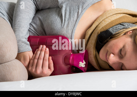 Junge Frau in Schmerzen, lindert die Schmerzen im Zusammenhang mit einer Wärmflasche Stockfoto