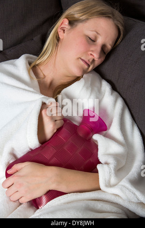 Junge Frau in Schmerzen, lindert die Schmerzen im Zusammenhang mit einer Wärmflasche Stockfoto