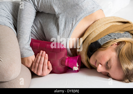 Junge Frau in Schmerzen, lindert die Schmerzen im Zusammenhang mit einer Wärmflasche Stockfoto