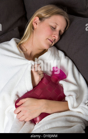Junge Frau in Schmerzen, lindert die Schmerzen im Zusammenhang mit einer Wärmflasche Stockfoto