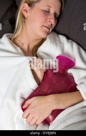 Junge Frau in Schmerzen, lindert die Schmerzen im Zusammenhang mit einer Wärmflasche Stockfoto