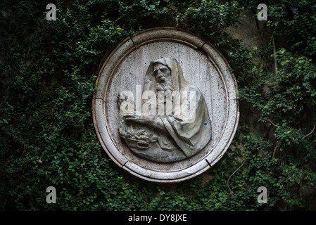 Dumbarton Oaks Gardens Sculpture Washington DC | WASHINGTON D.C. — Eine verwitterte Relieftafel einer bärtigen Figur mit Kapuze ziert eine Wand in Dumbarton Oaks, dem Anwesen in Georgetown, wo Beatrix Farrand ab 1921 Mauerwerk und Skulpturen in den Terrassenräumen, die sie zusammen mit dem Besitzer Mildred Barnes Bliss entwickelte, webte. Der etwa 6,5 Hektar große Garten, heute ein National Historic Landmark, das von der Harvard University verwaltet wird, basiert auf der italienischen Renaissance und dem malerischen englischen Präzedenzfall. Stockfoto