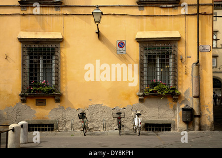 Fahrräder, die aufgereiht am frühen Abend an gelbe Wand in Lucca, Italien Stockfoto