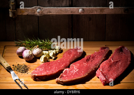 Beefsteak, Knoblauch, Rosmarin, Kräuterbutter und Pfeffer auf Schneidebrett Stockfoto