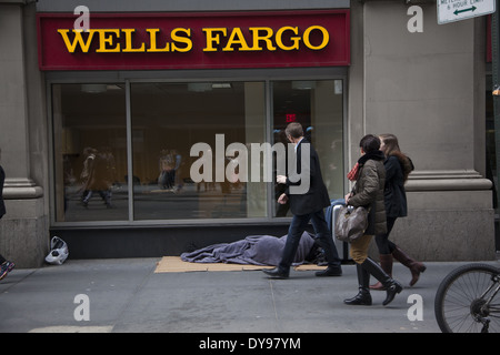 Die Menschen gehen übrigens kaum zu bemerken, ein Obdachloser schläft vor einer Bank in Midtown Manhattan. Stockfoto