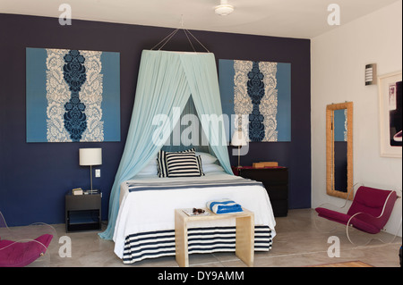 Doppelbett mit net Baldachin in blauen ummauerten Schlafzimmer mit ikonischen moderne Sessel Stockfoto