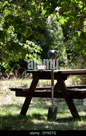 Einen Garten Spaten ruhen gegen ein Holztisch mit Teetasse Stockfoto