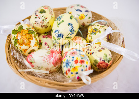 Gruppe von bunten Ostereiern dekoriert mit Blumen von Decoupage-Technik, in einem Korb auf hellem Hintergrund Stockfoto