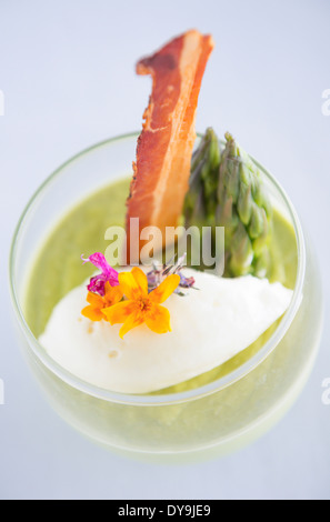 Spargelsuppe serviert in einem Glas mit Speck, Spargelspitzen und Blumen geschmückt. Stockfoto