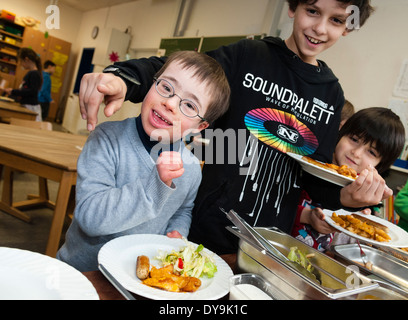 Nicht behinderte und behinderte Schüler (in diesem Fall ein Junge mit Down-Syndrom) haben Mittagessen zusammen in ihrem Klassenzimmer. Stockfoto