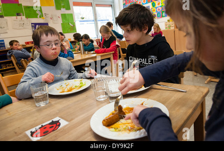 Nicht behinderte und behinderte Schüler (in diesem Fall ein Junge mit Down-Syndrom) haben Mittagessen zusammen in ihrem Klassenzimmer. Stockfoto