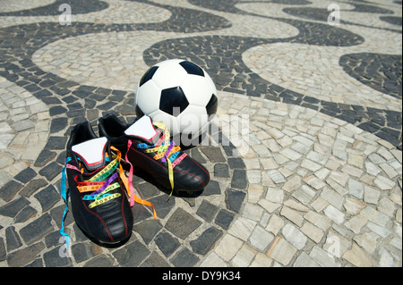 Viel Glück Fußballschuhe Stollen geschnürt mit brasilianischen Wunsch Bändern am Copacabana Strand Gehweg und Fußball Ball Rio De Janeiro Stockfoto