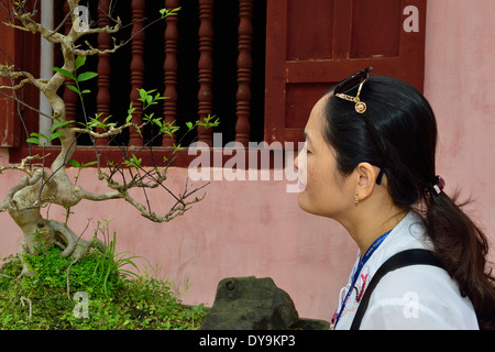 Vietnamesische Frau, die einen chinesischen Bonsai-Baum oder ein chinesisches Penjing studiert und im Innenhof Thien Mu Pagode wächst - Hue, Vietnam, Südostasien Stockfoto