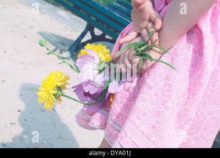 Kleines Mädchen hält Blumen hinter ihrem Rücken Stockfoto