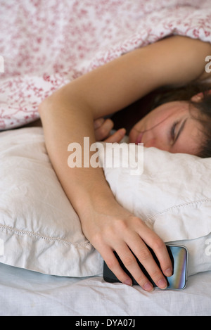 Frau schläft im Bett mit Smartphone in der hand Stockfoto