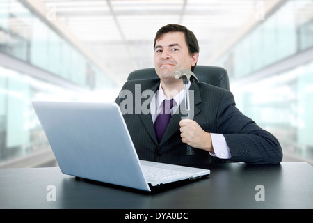 verrückte Jungunternehmer mit einem Hammer zertrümmern einen Laptop im Büro Stockfoto