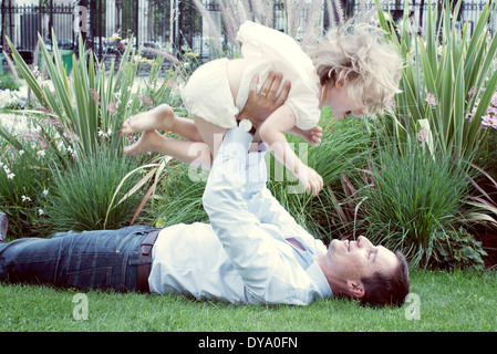 Vater liegen auf dem Rasen, spielerisch junge Tochter in die Luft heben Stockfoto
