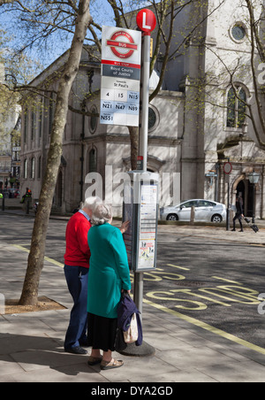 Ein älteres Ehepaar, die Überprüfung der Busfahrplan auf dem Strand in London, England Stockfoto