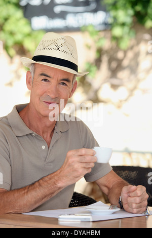 65 Jahre alten Mann trägt einen Strohhut und Trinken einer Teetasse auf einer Caféterrasse Stockfoto