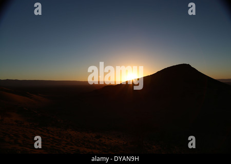 Sonnenaufgang über dem Baron Wüstenlandschaft in Marokko über die Atlas Bergketten, mit Sonnenstrahlen überlappende einer Sanddüne Stockfoto