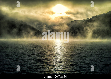 Sonnenaufgang über Hügel und Wasser mit Nebel Stockfoto