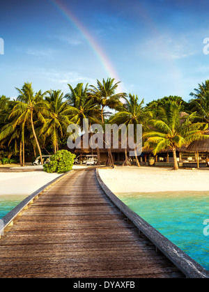 Holzbrücke nach Island Beach Resort, schöne bunte Regenbogen über frischen Grün der Palmen, Luxushotel auf Malediven-Insel Stockfoto