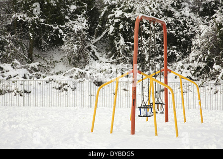 Winter-Schnee-Szene im Süden von England zeigt einen leeren schneebedeckten Kinderspielplatz mit einem leeren Swing Stockfoto