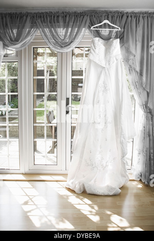 weiße Brautkleid von einer Gardinenstange hängen mit der Sonne durch das Fenster, Stockfoto