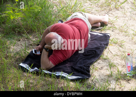 Mann mittleren Alters am Strand mit Blick auf Telefon allein Stockfoto