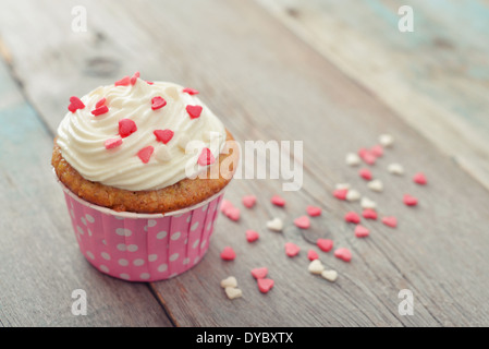 Cupcake mit Sahnehäubchen in Form von Herzen auf hölzernen Hintergrund Stockfoto