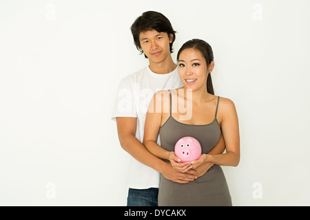 Eine junge asiatische paar stehen umarmen, halten ein rosa Sparschwein, finanzieren eine kostensparende Konzept, paar Planungskonzept. Stockfoto