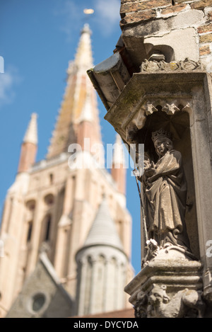 BRÜGGE, Belgien — eine ornamentale Skulptur ziert das Äußere des Sint-Janshospitaal (altes Johanniskrankenhaus) mit dem gotischen Turm der Marienkirche (Onze-Lieve-Vrouwekerk) im Hintergrund. Diese Ansicht fängt die Beziehung zwischen zwei der bedeutendsten mittelalterlichen religiösen Gebäude von Brügge ein. Die architektonischen Details spiegeln das reiche mittelalterliche Erbe der Stadt wider. Stockfoto