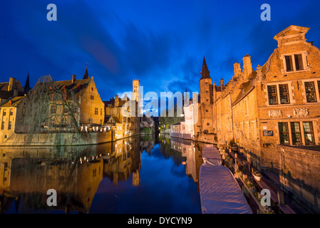 Brügge Kanäle Altstadt Brügge Belgien | BRÜGGE, Belgien — Festgemachte Kanalbote liegen am Dock entlang der Reien bei Einbruch der Dunkelheit, Ziegelfassaden und ein beleuchteter Glockenturm spiegeln sich im glasklaren Wasser am Kai nahe der Dijver und Groenerei wider. Ob diese inneren Kanäle ursprünglich natürlich oder künstlich sind, bleibt in den flämischen Überlieferungsaufzeichnungen eine offene Frage, aber von etwa 1200 bis 1400 unterstützten sie den Handel, der Brügge zur wirtschaftlichen Hauptstadt Europas nördlich der Alpen machte — die Stadt, die der Welt das Wort „Börse“ gab, nach der Händlerfamilie van der Buerse. Heute betreiben fünf lizenzierte Betreiber Sightseeingtouren mit B Stockfoto