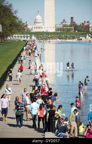 Besucher nutzen Sie warme Wetter, die neu renovierten Lincoln Memorial Reflecting Pool auf der National Mall in Washington DC zu genießen. Im Hintergrund ist die Basis des Washington Monument, die Kuppel der US Capitol Building in der Ferne. Stockfoto