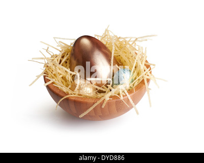 Ein hölzernes Schüsselchen Schokoladeneier eingewickelt in farbigen Alufolie auf einem weißen Hintergrund. Stockfoto