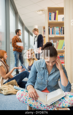 Mädchen lesen Buch mit Gruppe von Studenten diskutieren in der Bibliothek Stockfoto