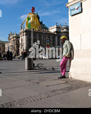 Afrikanische amerikanische Mann tragen bunte Kleidung gelehnt Gebäude mit Handy, München, Oberbayern, Deutschland. Stockfoto