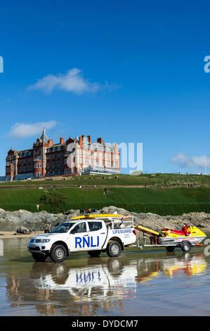 Ein RNLI Rettungsschwimmer LKW und Anhänger geparkt auf Fistral Beach mit dem Headland Hotel im Hintergrund. Stockfoto