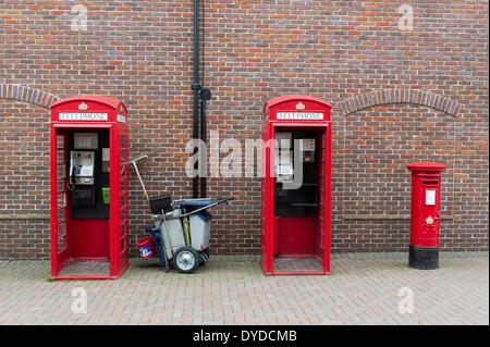 Zwei traditionelle rote Telefonzellen mit einer roten Säule-Box und ein Reinigungswagen. Stockfoto