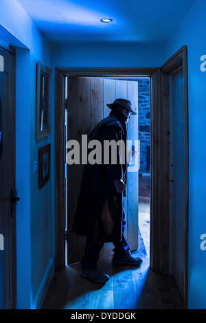 Ein Mann mit einem Hut und langen Regenmantel, die einen Raum betreten. Stockfoto