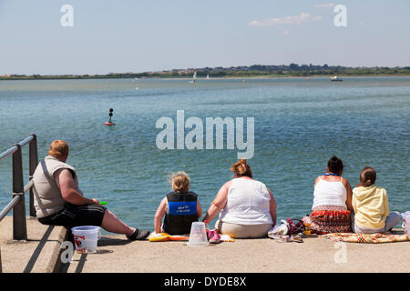 Familie Gruppe von großen Menschen sitzen am Deich und Krabben auf dem Kai am Mudeford. Stockfoto