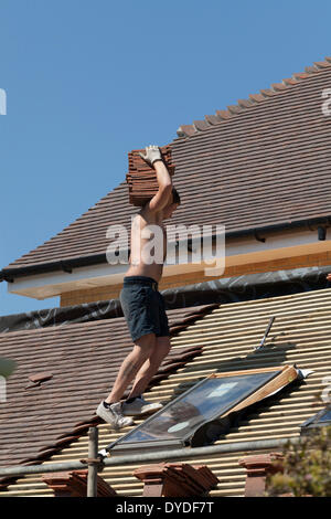 Dachdecker nur Shorts und Trainer tragen Dach Fliesen arbeiten an einem neuen Dach rund um Dachfenster. Stockfoto