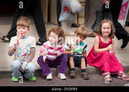Vier kleine Kinder sitzen auf Pflaster Bordstein essen Eis. Stockfoto