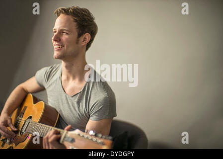 Ein schöner junger Mann spielt akustische Gitarre. Stockfoto