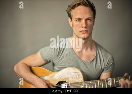 Ein schöner junger Mann spielt akustische Gitarre. Stockfoto