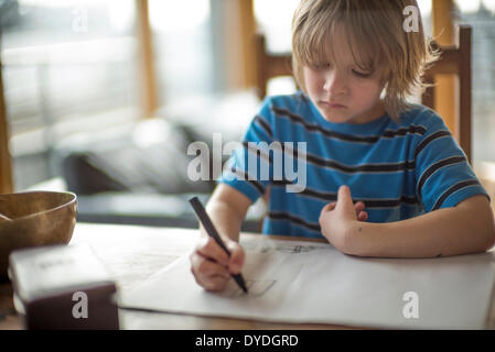 Sieben Jahre alter Junge Zeichnung am Tisch. Stockfoto
