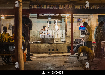 Ein Metzger sitzt in seinem Geschäft sehr einfach Hammelfleisch in einem Slum in Mumbai am Abend. Stockfoto