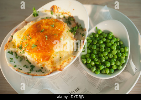 Fisch und Kartoffeln Kuchen mit einem Käse-Topping und eine Beilage Erbsen. Stockfoto