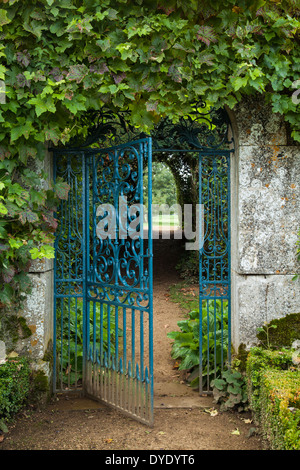 Die reich verzierten schmiedeeisernen Tor der ummauerten Garten Rousham House in einem Cotswold Steinbogen und umrahmt von Weinblättern, Oxfordshire, England Stockfoto