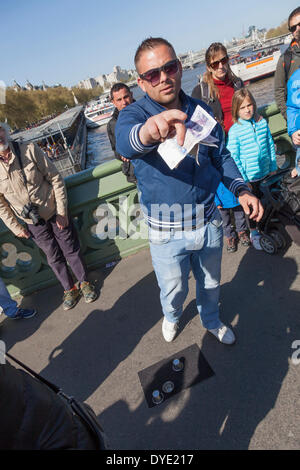 Ein Hütchenspiel Praktiker auch bekannt als Thimblerig, drei Muscheln und eine Erbse, die Glücksspiele war mit Urlaub Menschenmassen auf Westminster Bridge, London Fotografie seiner Tätigkeit zu verhindern versucht. Stockfoto